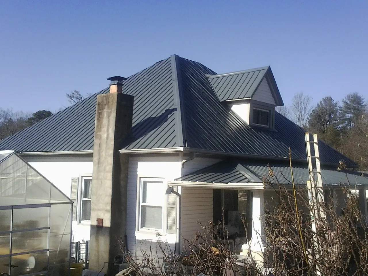 Dark blue standing seam metal roof on a white farmhouse with dormer — Slate & Tile Roof Repair by Roofing Brothers in Altmar