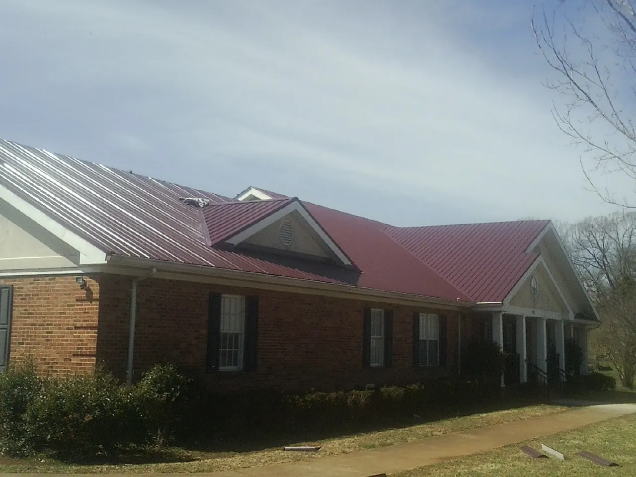 Red metal roof with gabled entries on a long brick building, from a Hail Damage Roof Repair job in Altmar