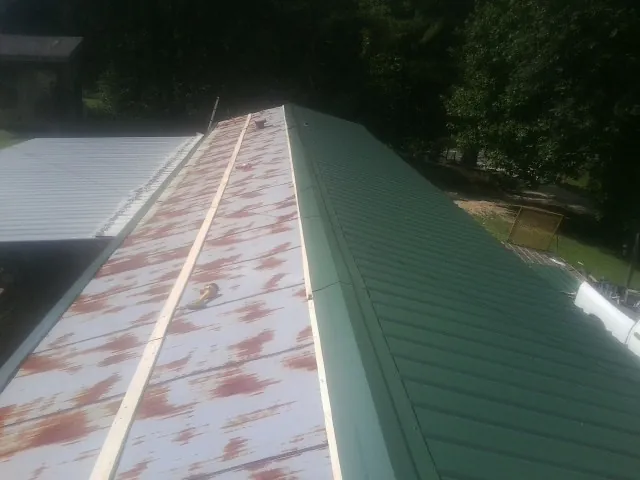 Old rusted panels beside newly installed green metal roofing — Wind Damage Roof Repair by Roofing Brothers in Altmar