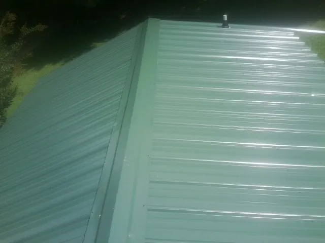 New green metal panels meeting at the ridge of a roof — Flat Roof Repair work by our crew in Altmar