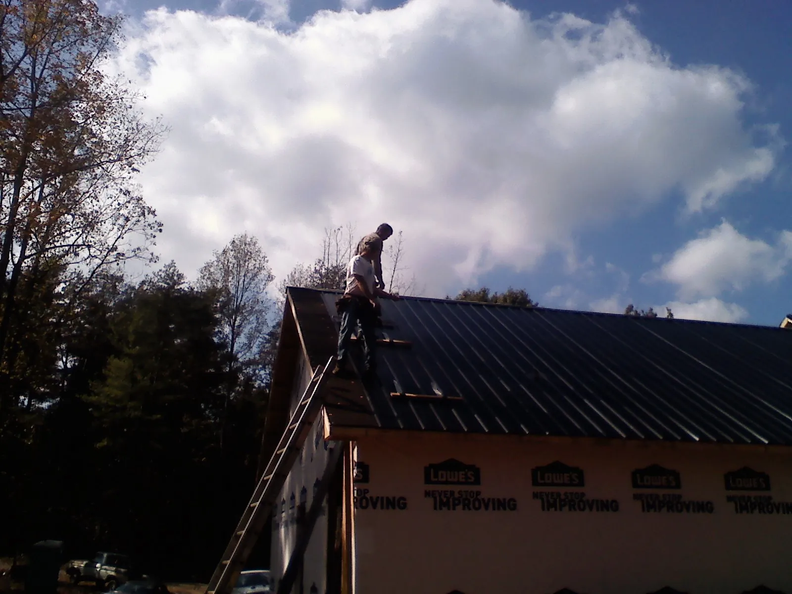 Roofer fastening dark metal panels high against a cloudy sky, from a Roof Inspection job in Altmar