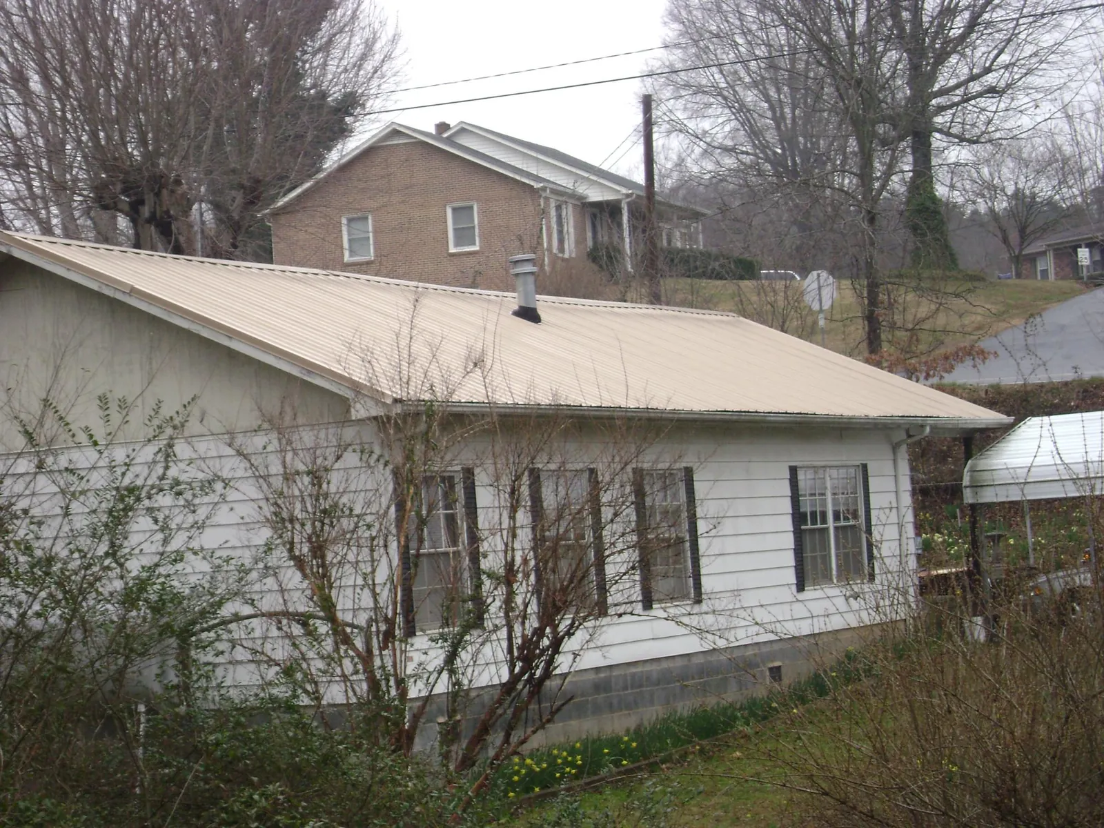Tan metal roof on a white sided house set into a hillside — Commercial Roofing by Roofing Brothers in Altmar
