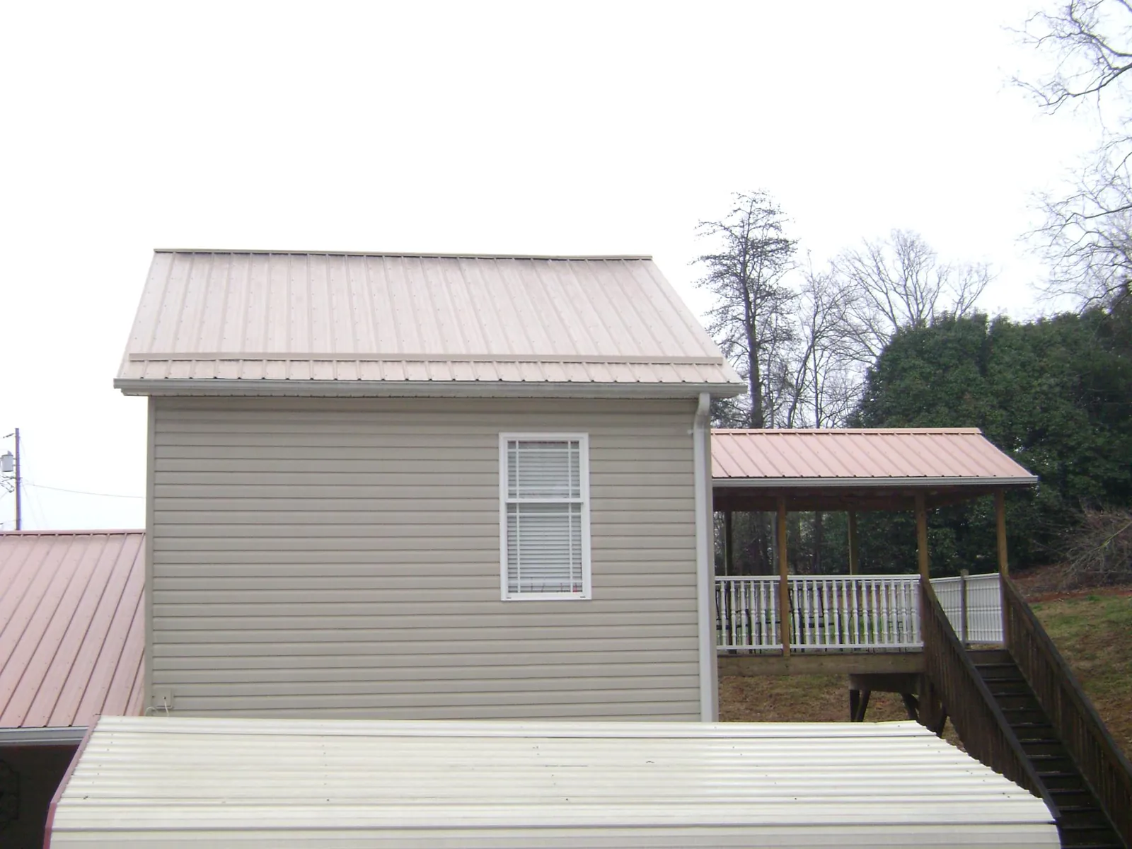 Tan metal roofs on a two story addition and attached porch, from a Roof Replacement job in Altmar
